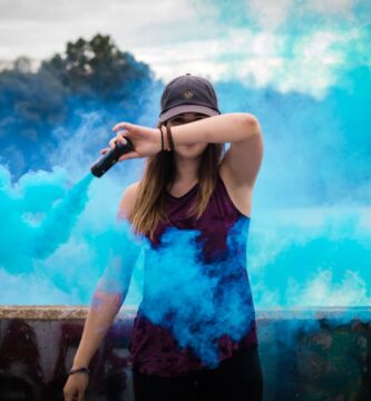 A stylish woman surrounded by bright blue smoke outdoors, creating a dynamic fashion statement.